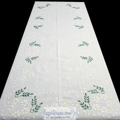 a white table cloth with green and yellow flowers on it's edges, sitting on a black surface