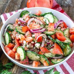 a white bowl filled with cucumber, tomato and onion salad on top of a wooden table