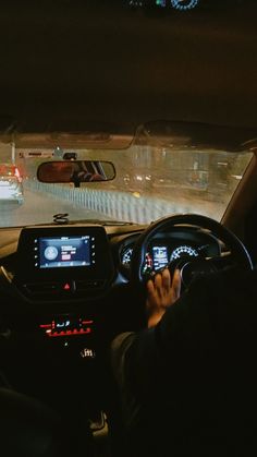 a person driving a car at night with their hands on the steering wheel and dashboard