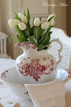 white tulips in a red and white vase on a table with lace napkins