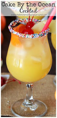 a yellow cocktail with a cherry garnish on the rim and topped with sprinkles