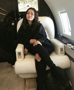 a woman sitting in an airplane seat with her legs crossed and wearing black over the knee boots