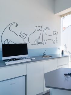 a computer on top of a desk in front of a wall with cats drawn on it