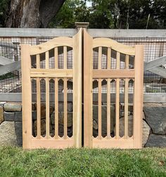 two wooden gates sitting in the grass next to a stone wall and fenced in area