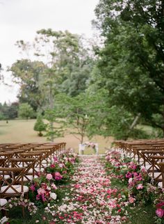 the aisle is lined with wooden chairs and pink flowers on the grass in front of them