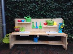 a wooden bench with pots and pans on top of it in front of a hedge