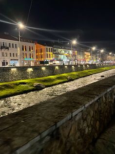 a city street at night with lights on and green grass growing along the side of the road