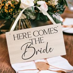 there is a sign that says here comes the bride next to some flowers on a table