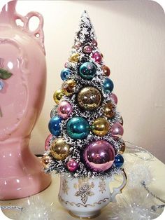 a small christmas tree sitting next to a pink vase with ornaments on it's side