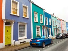 a car parked on the side of a street in front of colorful houses with windows