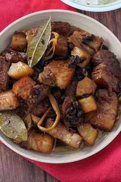 a bowl filled with meat and vegetables on top of a wooden table next to a red napkin