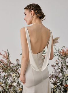 the back of a woman in a white dress standing next to some flowers and grass