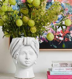 a vase filled with flowers sitting on top of a table next to books and a painting