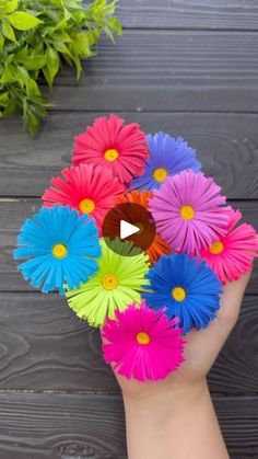 a hand holding colorful paper flowers on top of a wooden table