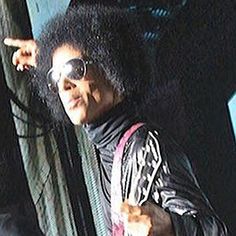 a man with an afro pointing at something in the air while wearing sunglasses and a leather jacket