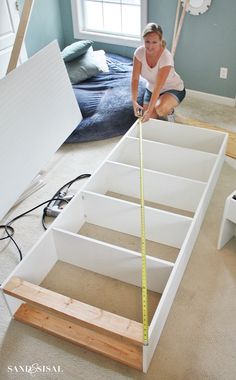 a woman measuring the width of a bed frame with a tape measure in front of her