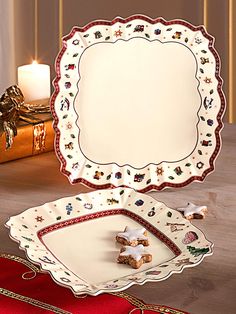 two plates with christmas decorations on them next to a lit candle and gift box in the background