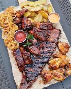 barbecue ribs, fries and coleslaw are on a paper towel next to some dipping sauce