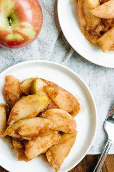 two white plates topped with apple slices next to silverware and an apple on a table