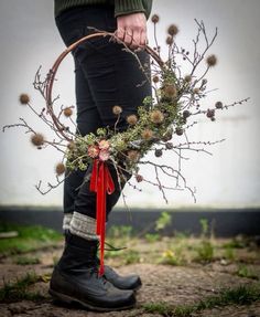 a person wearing boots and holding a twig wreath with red ribbon tied to it