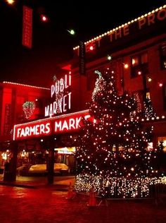 a christmas tree is lit up in front of a farmers market at night with lights on it