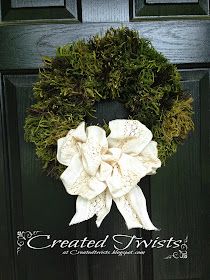 a wreath is hanging on the front door with white fabric and greenery around it