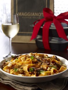 a bowl of pasta with meat and vegetables next to a glass of wine