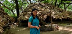 a woman standing in front of a hut with thatched roof