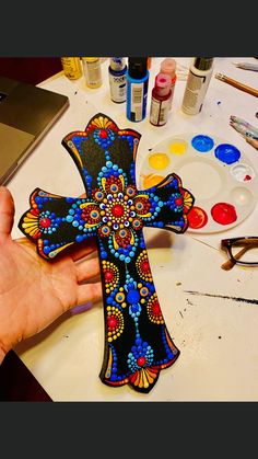 a person holding up a painted cross on a table