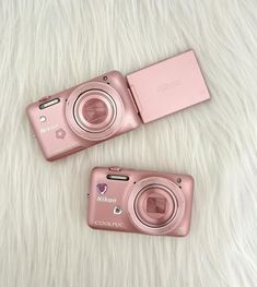 two pink cameras sitting next to each other on a white fur covered surface with the same object in front of them