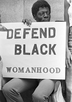 two people holding a sign that says defend black womanhood