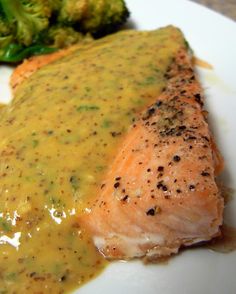 a piece of salmon covered in sauce and broccoli on a plate with gravy