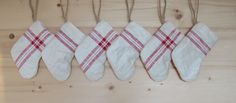 five white and red striped kitchen mitts hanging on a wooden wall with twine