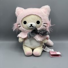 a pink stuffed animal with a bow on it's head and ears, sitting next to a tag