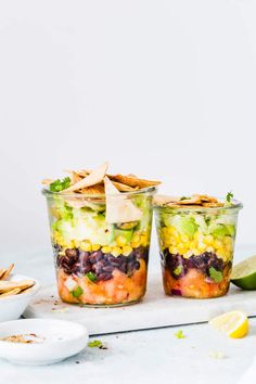 two glasses filled with mexican salad and tortilla chips on a white countertop