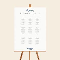 an easel with a wedding seating chart on it, sitting in front of a white wall