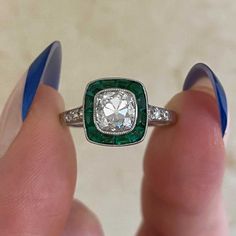 a woman's hand holding a ring with a diamond and emerald in the center