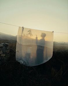 two people standing next to each other in the grass with a net hanging from them