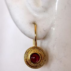 Handcrafted of a tiny disc of filigree thread, this classic Greek design highlights the beauty of a single cabochon garnet. The original Greek earrings are part of the Museum's permanent collection. 14k gold settings. Hinged backs for pierced ears. Size: 7/8 Inches. Elegant Gold Garnet Cabochon Jewelry, Gold Ruby Round Earrings, Byzantine Style Round Gemstone Jewelry, Byzantine Round Hallmarked Jewelry, Byzantine Jewelry With Cabochon For Gifts, 22k Gold Gemstone Round Earrings, Byzantine Style Gold-plated Round Jewelry, Byzantine Cabochon Jewelry For Gifts, Byzantine Style Cabochon Jewelry For Gifts