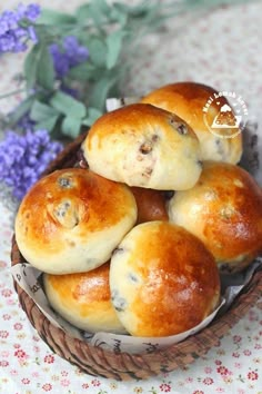 a basket filled with rolls sitting on top of a table next to a purple flower