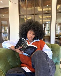 a person sitting on a couch with a book in their lap and an afro hair style