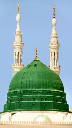 a green dome on top of a building with two minalis in the background and a blue sky behind it