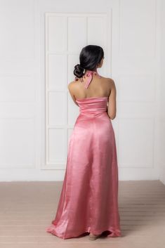 the back of a woman in a long pink dress standing against a white wall and looking off into the distance