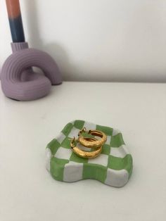 two gold rings sitting on top of a green and white checkered tray