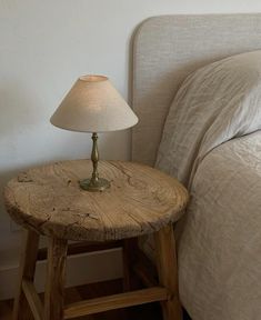 a wooden table with a lamp on top of it next to a neatly made bed