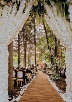 an outdoor wedding ceremony with white flowers and greenery on the aisle, surrounded by tall trees