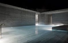 an indoor swimming pool in the middle of a building at night with lights shining on it