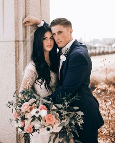 a bride and groom standing next to each other in front of a wall with flowers