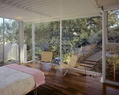 a bedroom with wooden floors and large windows overlooking the trees outside, is shown in this image