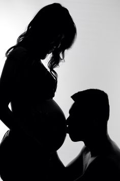 a pregnant woman kissing her husband's cheek in silhouette against a white background,